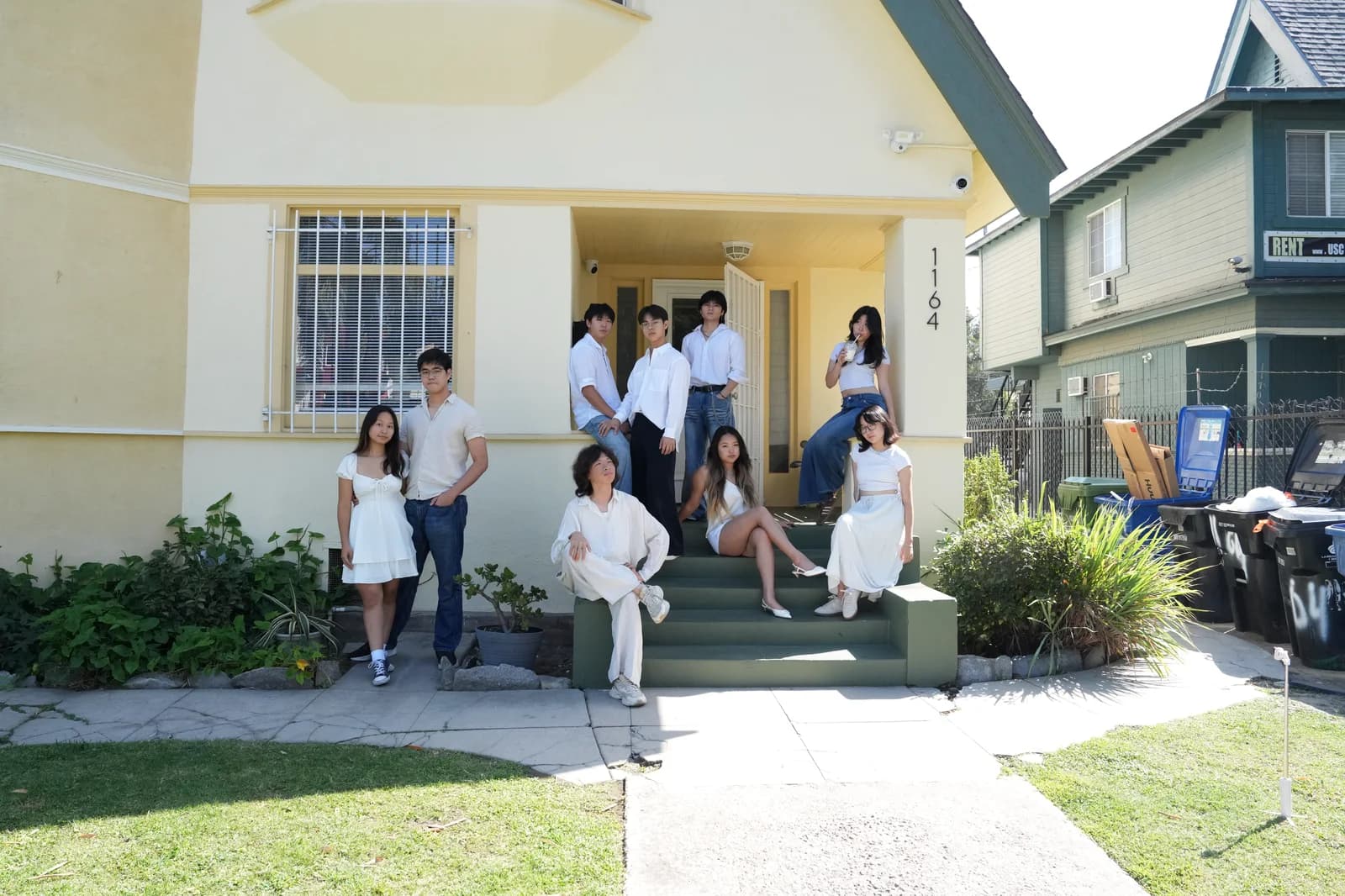Nine friends dressed in white arranged across the front steps of a yellow house