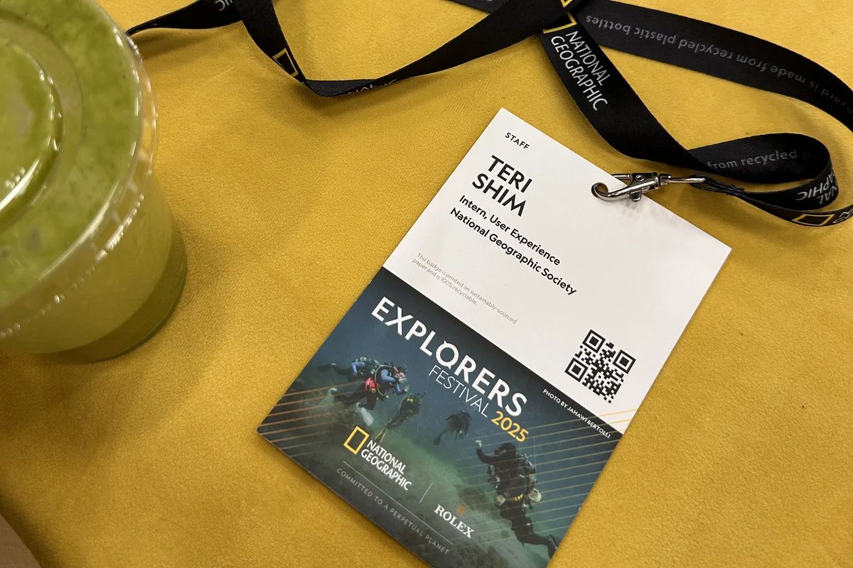 A National Geographic staff badge reading Teri Shim, Intern, User Experience, on a yellow jumper beside its lanyard