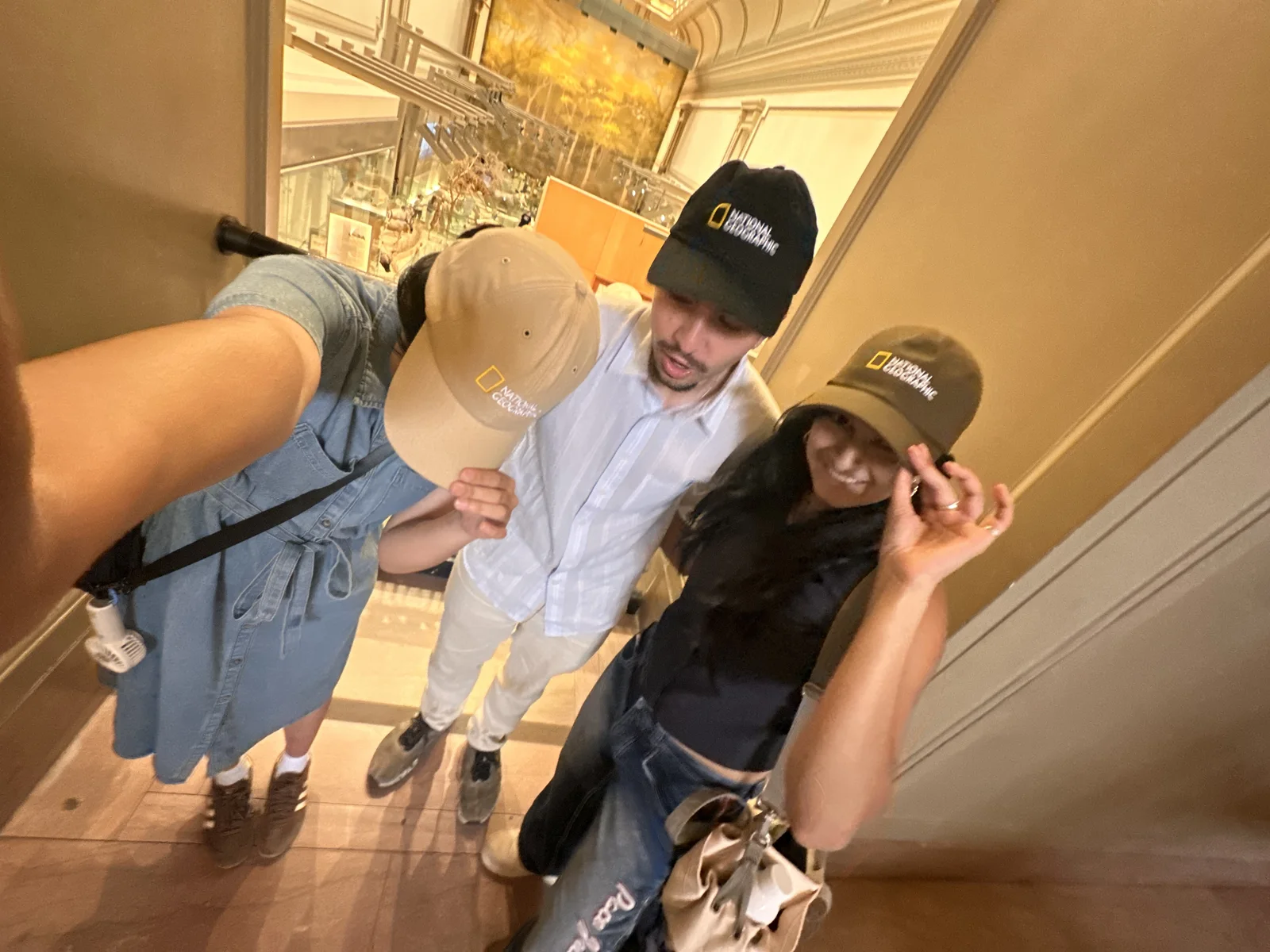 Three National Geographic interns in branded caps, taking a selfie in a museum hall