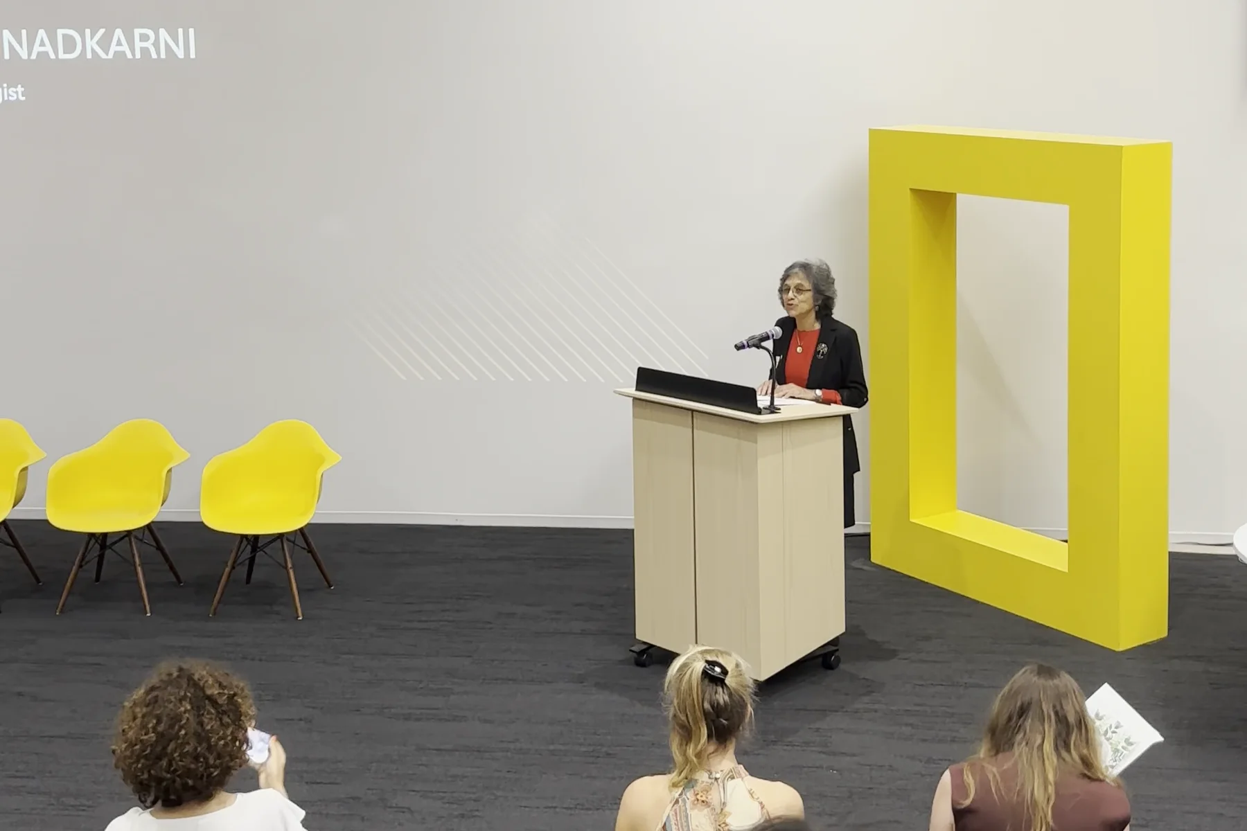 A talk at the Explorers Festival, seen from the back of the room: a speaker at a podium beside the Society's yellow rectangle, standing six feet tall