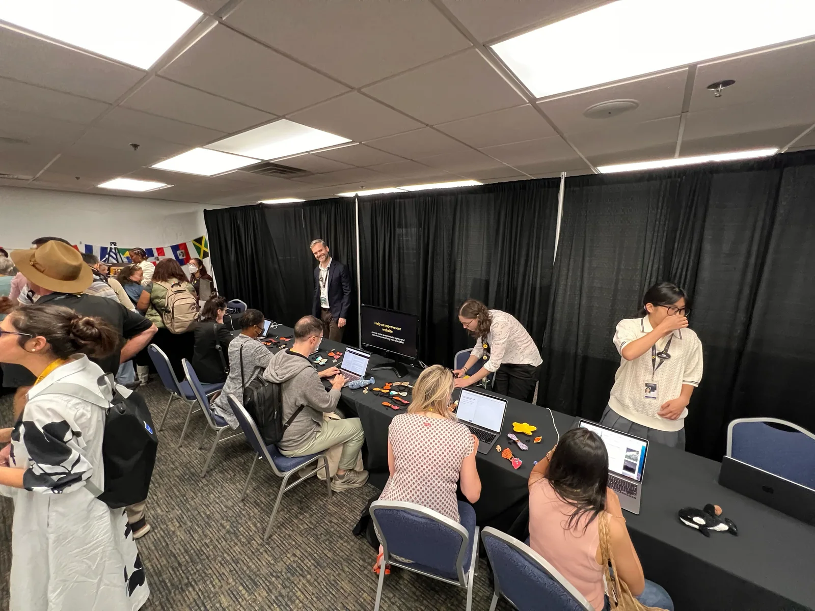 A room at the Explorers Festival with people seated at laptops testing, facilitators standing over them
